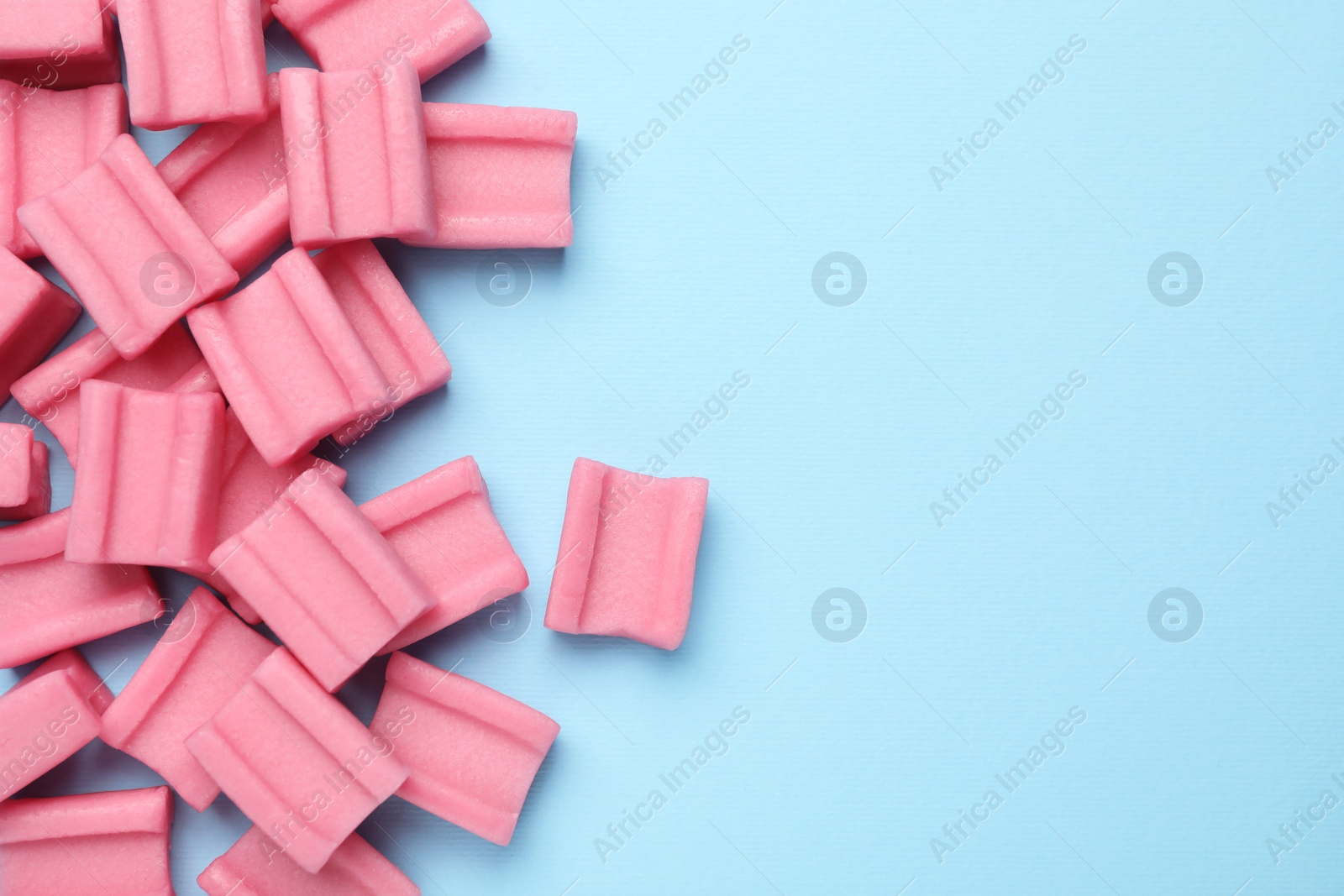 Photo of Tasty pink chewing gums on light blue background, flat lay. Space for text