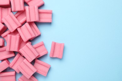 Photo of Tasty pink chewing gums on light blue background, flat lay. Space for text