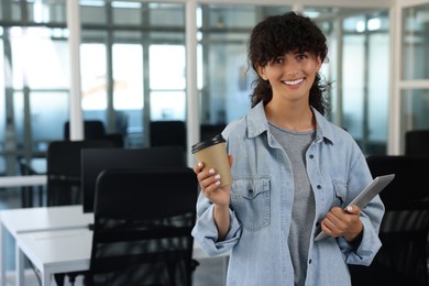 Photo of Happy woman with paper cup of drink and tablet in office, space for text