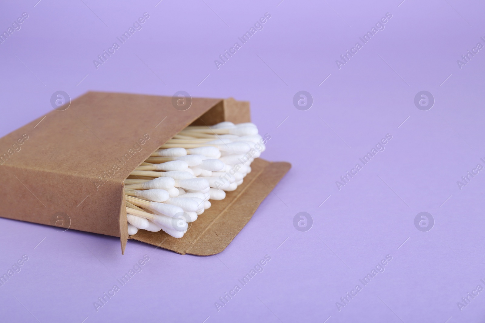 Photo of Box with wooden cotton buds on violet background. Space for text