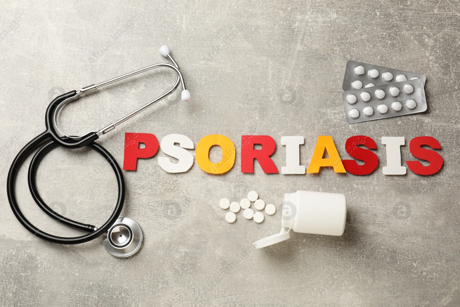 Photo of Word Psoriasis made of paper letters, stethoscope and pills on light gray textured table, flat lay