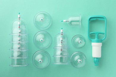 Photo of Plastic cups and hand pump on turquoise background, flat lay. Cupping therapy