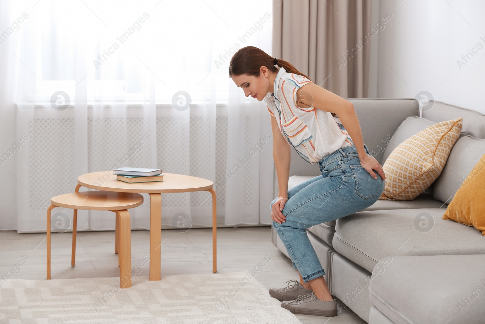 Photo of Young woman suffering from hemorrhoid on sofa at home
