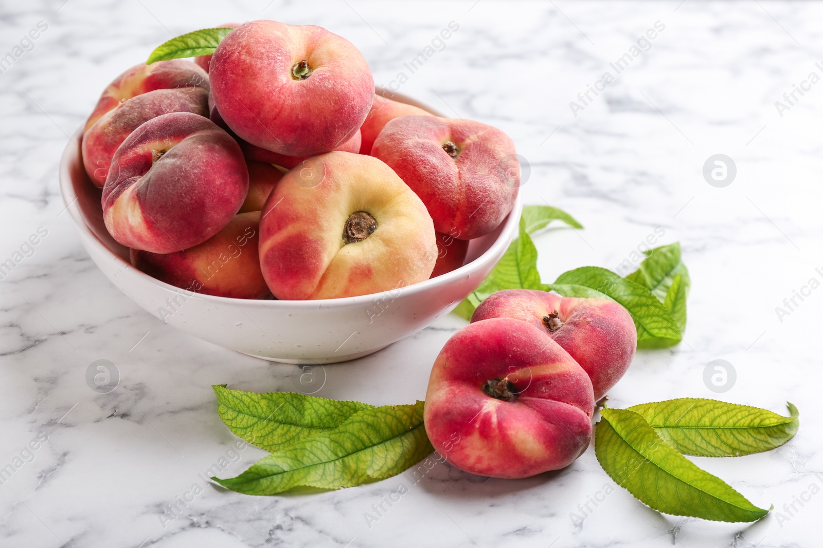 Photo of Fresh ripe donut peaches with leaves on white marble table