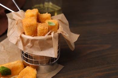 Photo of Metal basket with tasty fried mozzarella sticks on wooden table, closeup. Space for text