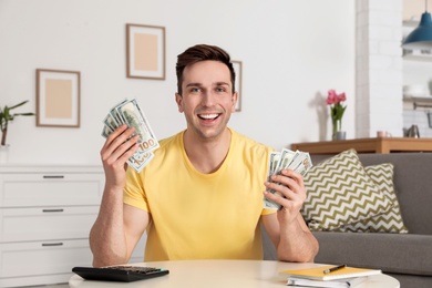 Happy man with money at table in living room