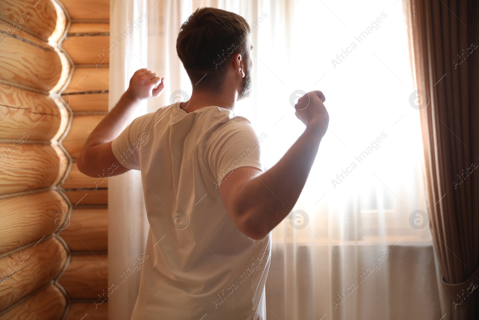 Photo of Man stretching near window indoors. Lazy morning