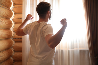 Man stretching near window indoors. Lazy morning