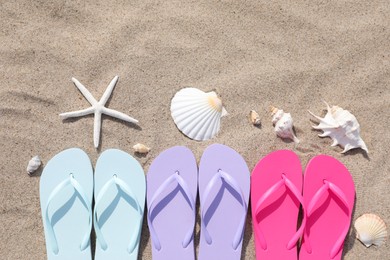 Photo of Stylish colorful flip flops, starfish and seashells on sand outdoors, flat lay. Space for text