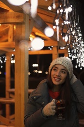 Woman with glass cup of mulled wine at winter fair. Space for text