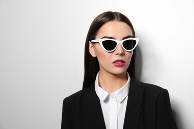 Young businesswoman in stylish sunglasses on light background