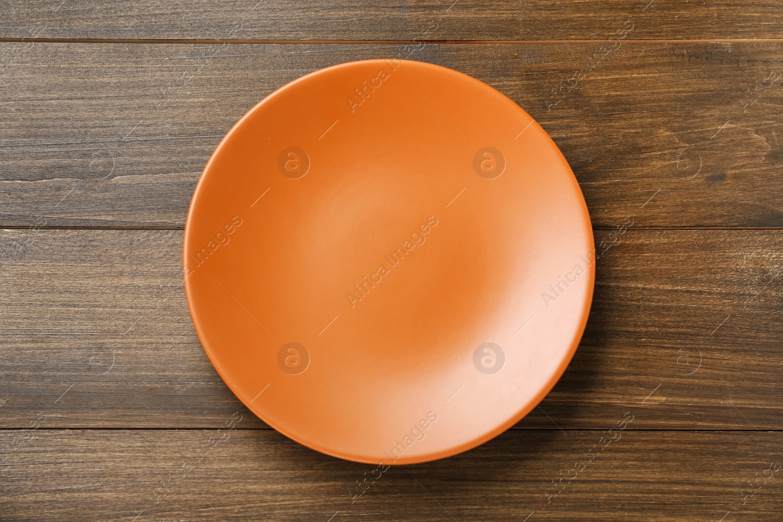 Photo of Empty orange ceramic plate on wooden table, top view