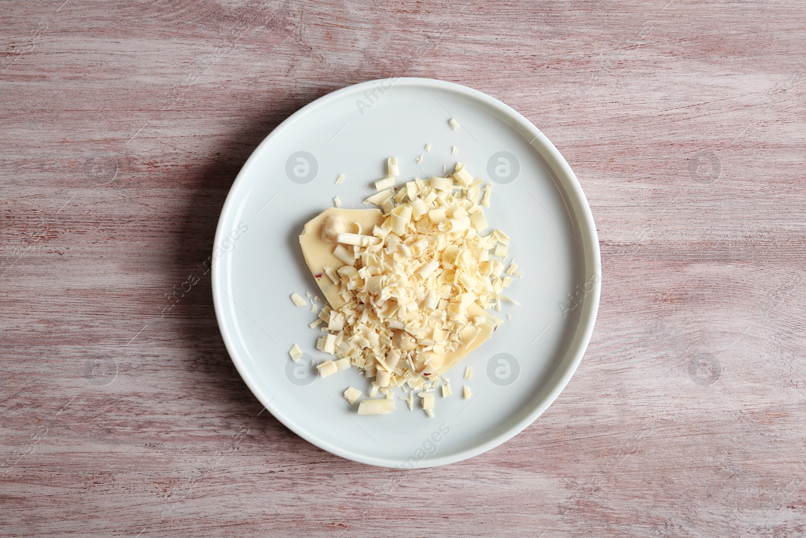 Photo of Plate with white chocolate curls on wooden background, top view