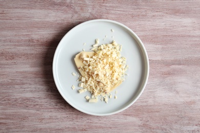 Plate with white chocolate curls on wooden background, top view