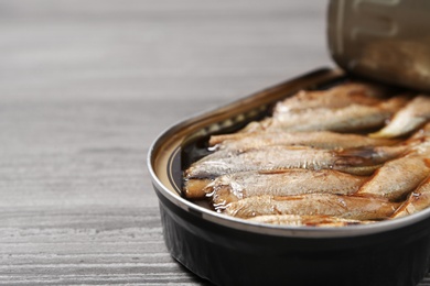 Open tin can with sprats on wooden table, closeup. Space for text