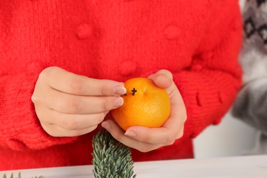 Photo of Woman decorating fresh tangerine with cloves, closeup. Making Christmas pomander ball