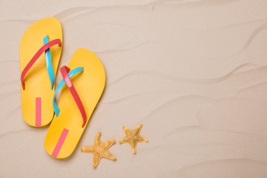 Photo of Pair of yellow flip flops and starfishes on sand, flat lay. Space for text