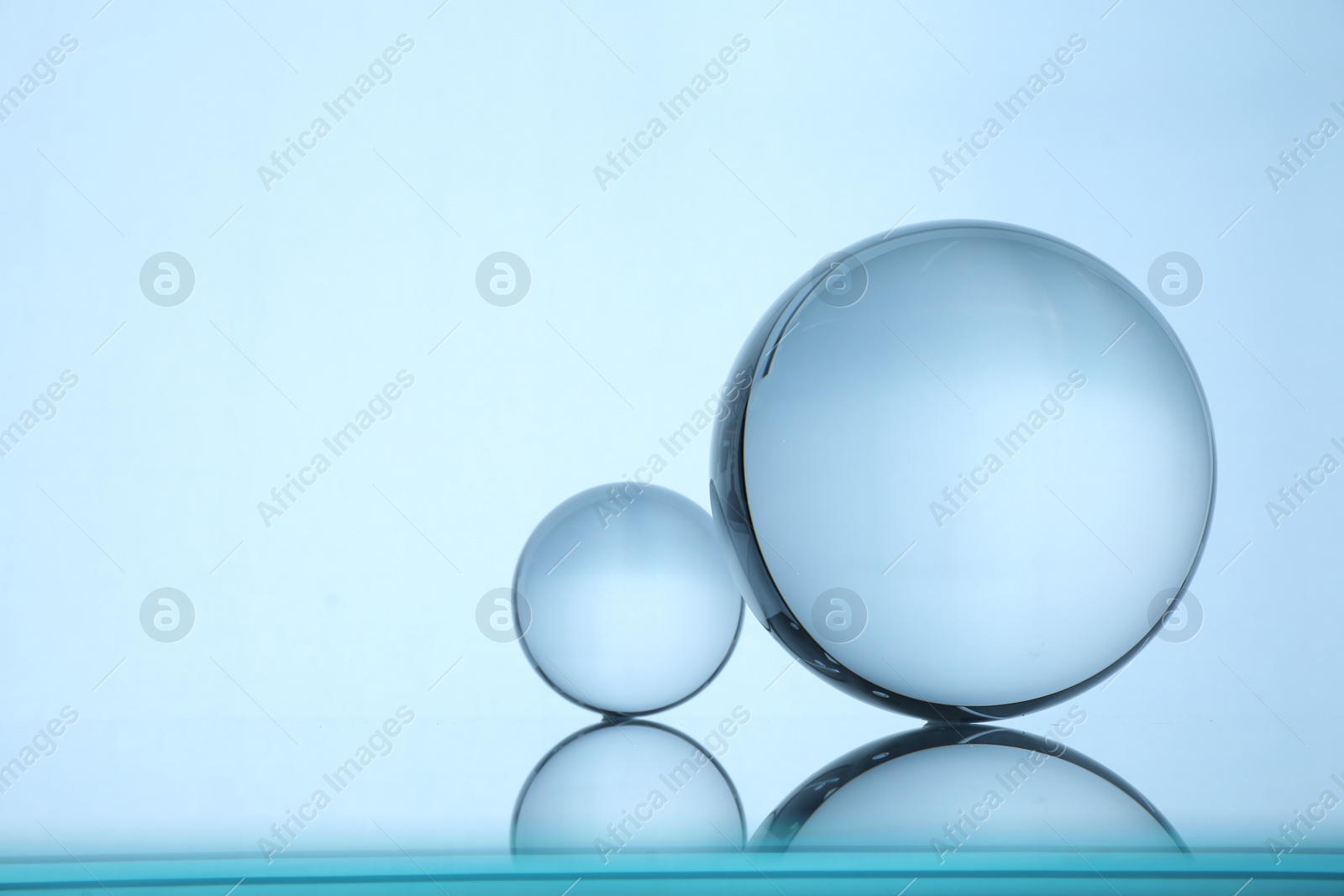 Photo of Transparent glass balls on mirror surface against light background. Space for text