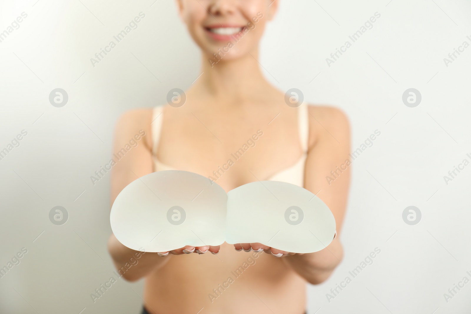 Photo of Woman holding silicone implants for breast augmentation on white background, closeup. Cosmetic surgery