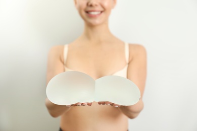 Woman holding silicone implants for breast augmentation on white background, closeup. Cosmetic surgery