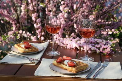 Photo of Delicious Belgian waffles with fresh strawberries and wine served on table in spring garden