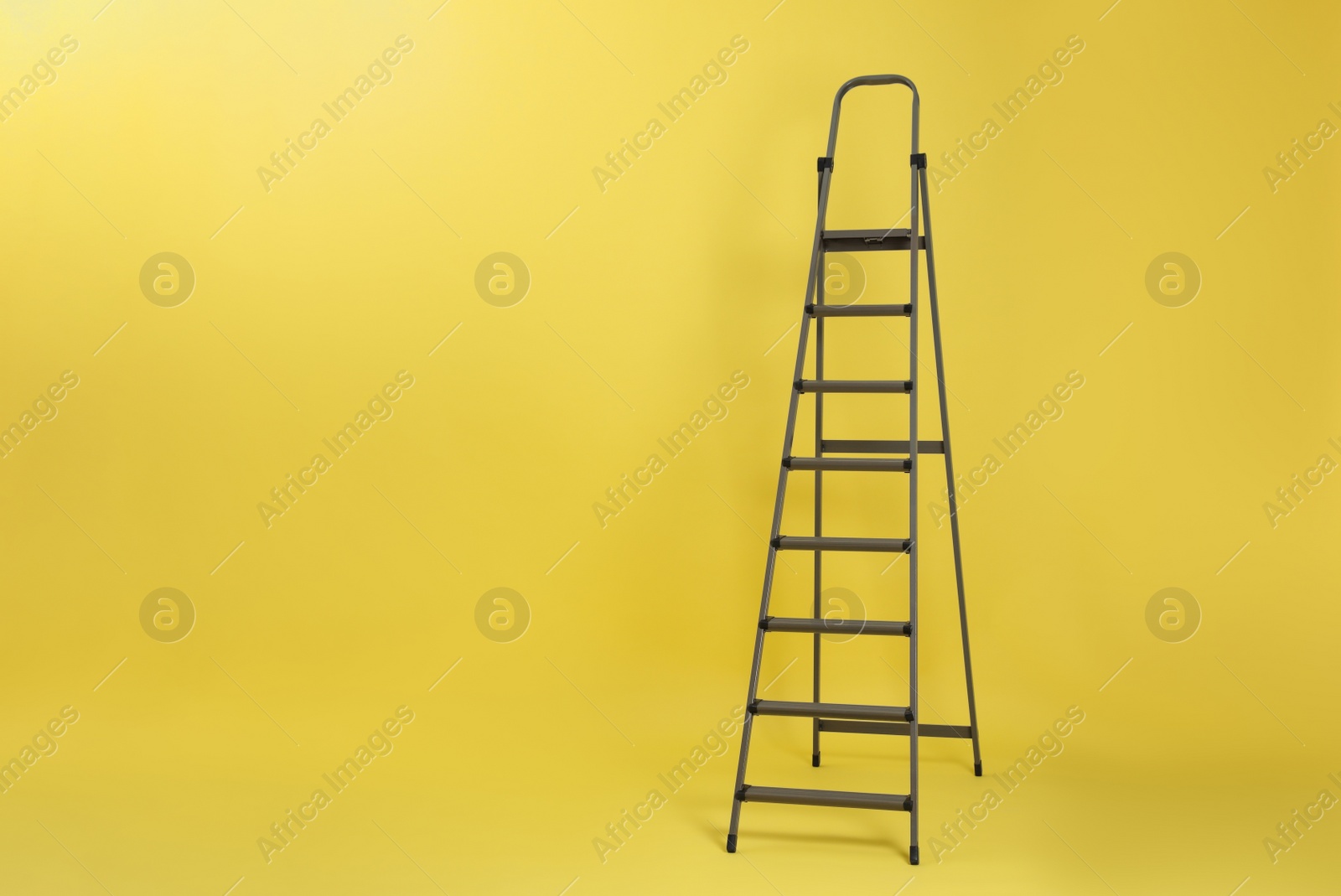 Photo of Metal stepladder on yellow background. Space for text