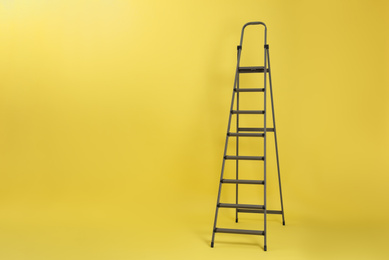Photo of Metal stepladder on yellow background. Space for text