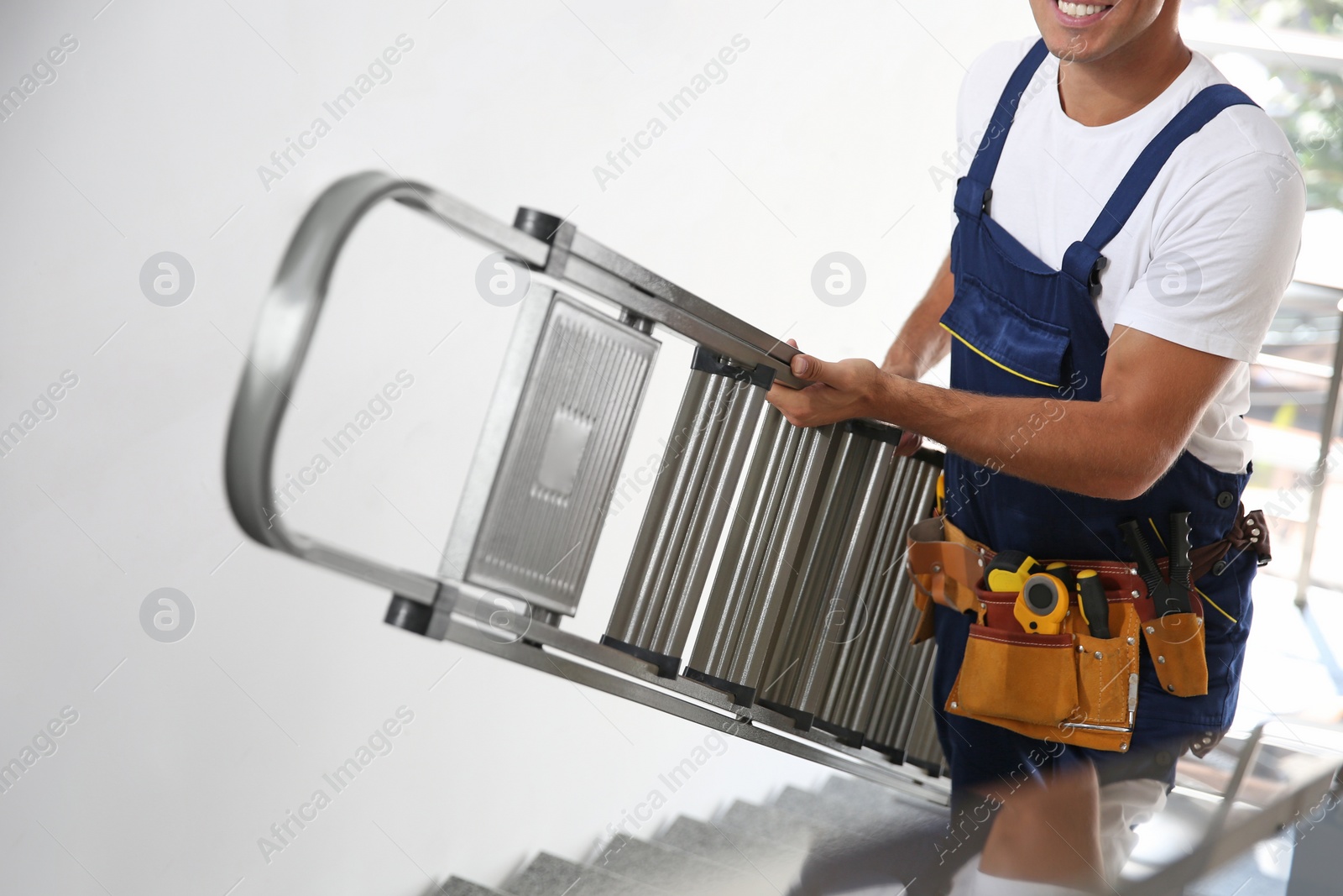Photo of Professional builder carrying metal ladder up stairs, closeup