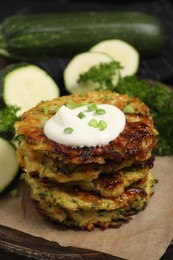 Photo of Delicious zucchini fritters with sour cream on board, closeup