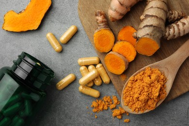 Photo of Aromatic turmeric powder, pills and raw roots on grey table, flat lay
