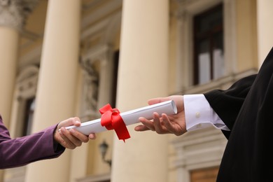 Student receiving diploma during graduation ceremony outdoors, closeup