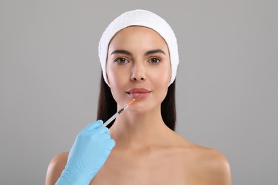 Doctor giving lips injection to young woman on light grey background. Cosmetic surgery