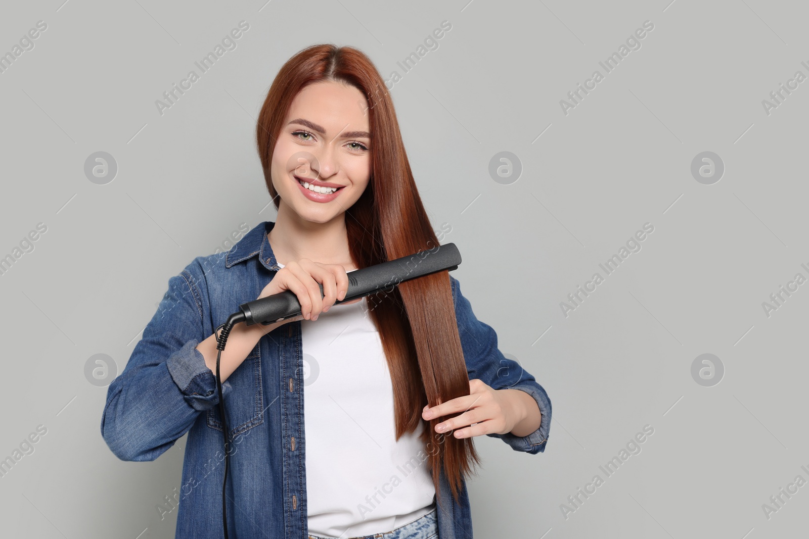 Photo of Beautiful woman using hair iron on light gray background, space for text