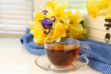 Photo of Cup of aromatic tea, beautiful yellow daffodil and iris flowers on windowsill. Space for text