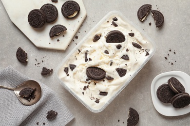 Flat lay composition with container of ice cream and chocolate cookies on grey background