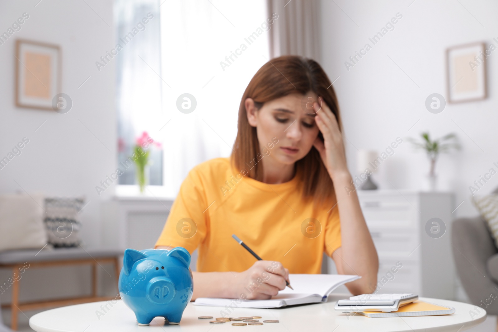 Photo of Sad woman with piggy bank and money at table indoors