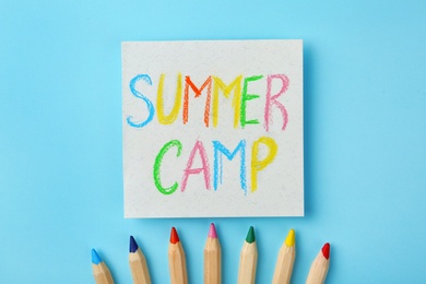 Paper with written text SUMMER CAMP and different pencils on color background, flat lay