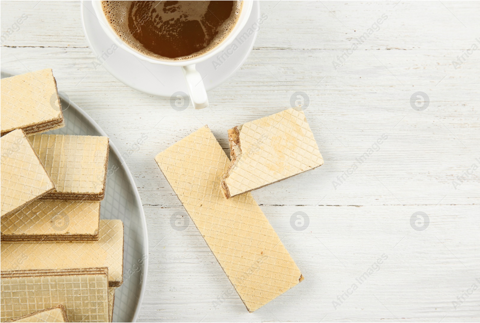 Photo of Plate of delicious wafers with cup of coffee on white wooden background, top view. Space for text