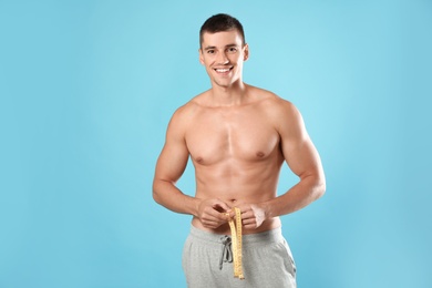 Photo of Young man with slim body using measuring tape on light blue background