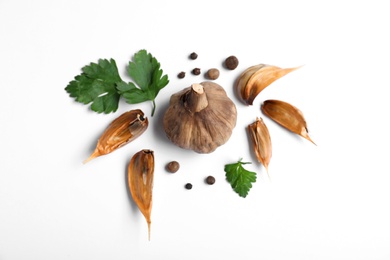 Aged black garlic with parsley and peppercorns on white background, view from above