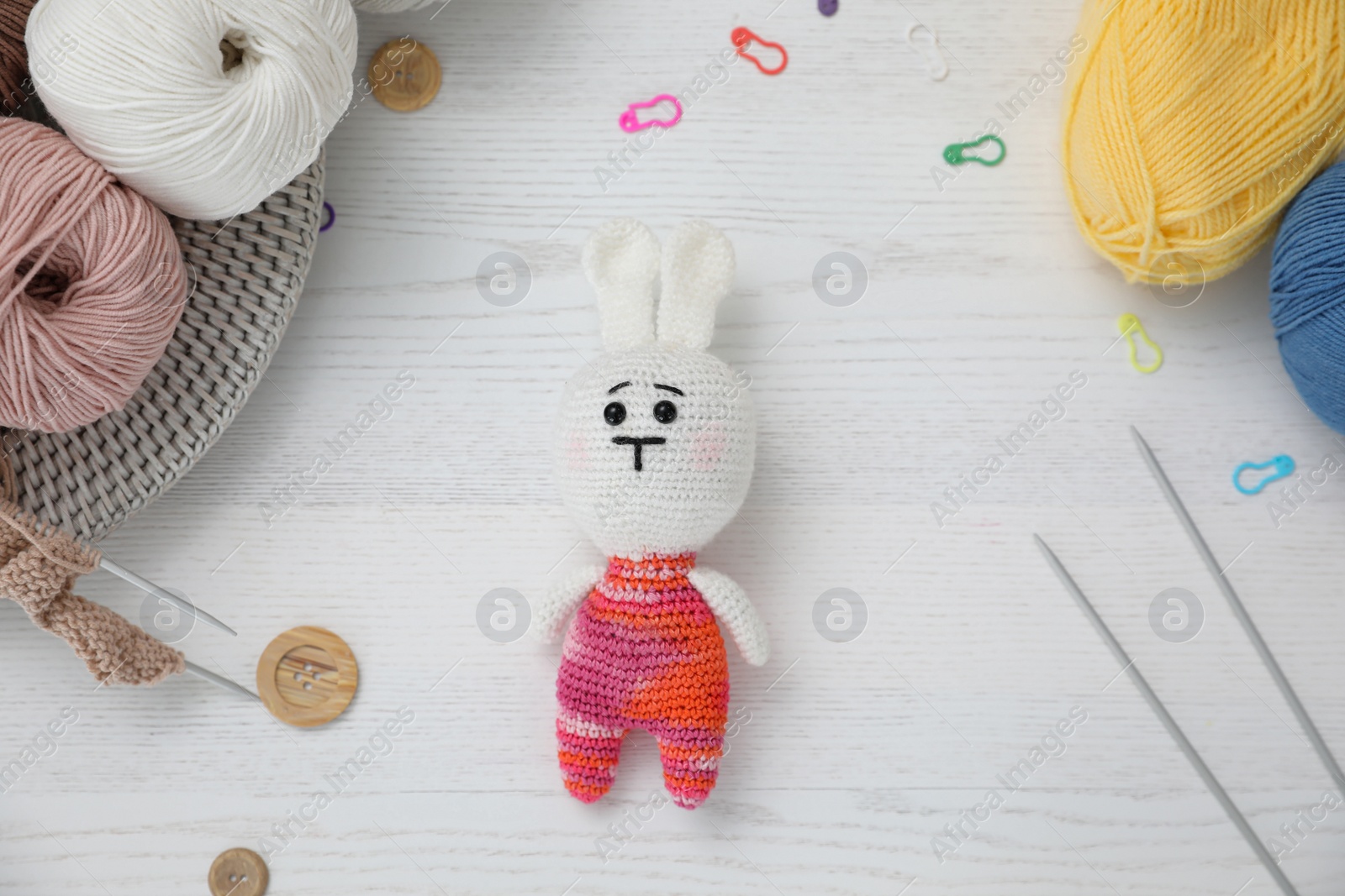 Photo of Crocheted bunny and knitting supplies on white wooden table, flat lay. Engaging in hobby