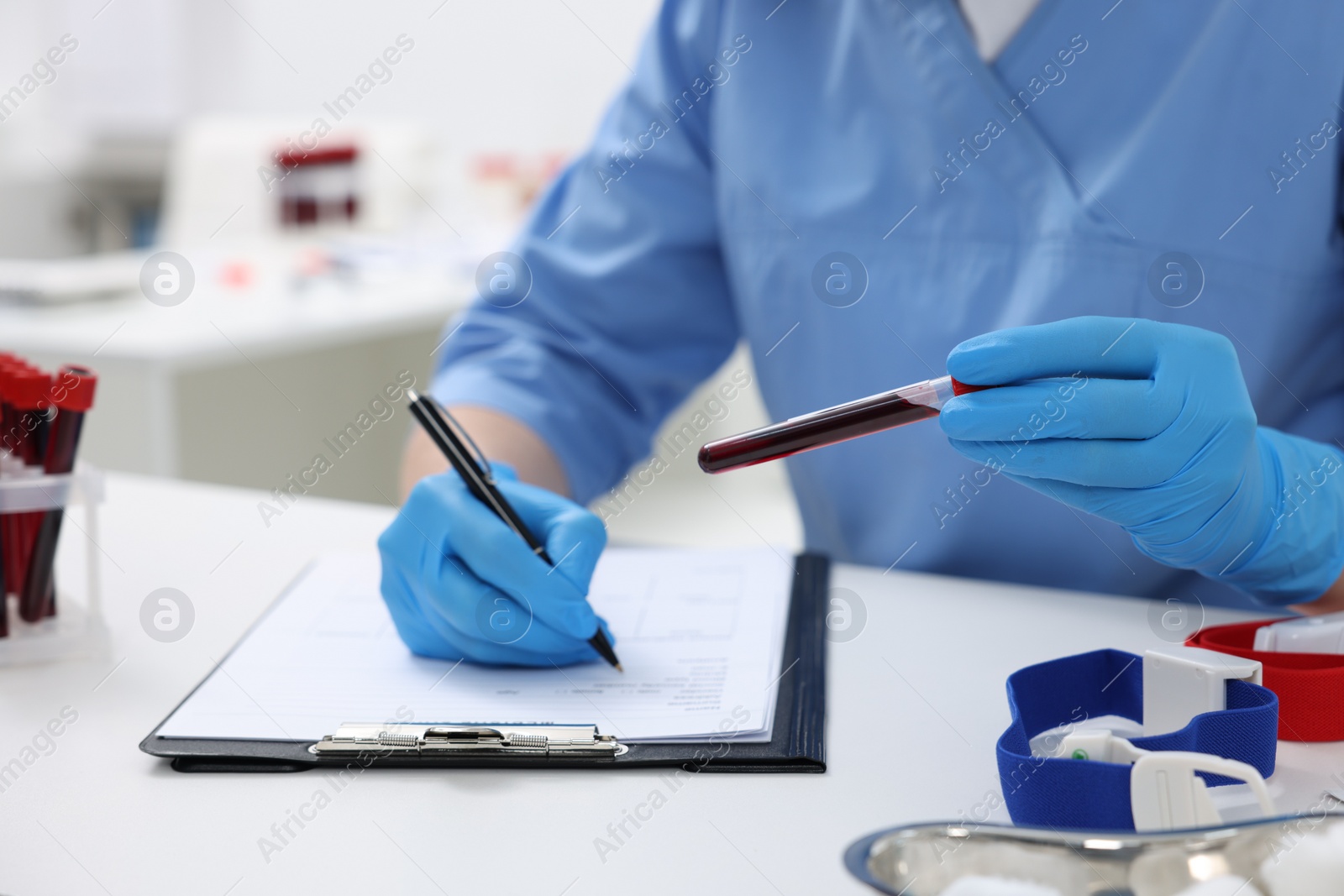 Photo of Laboratory testing. Doctor with blood sample in tube at white table indoors, closeup