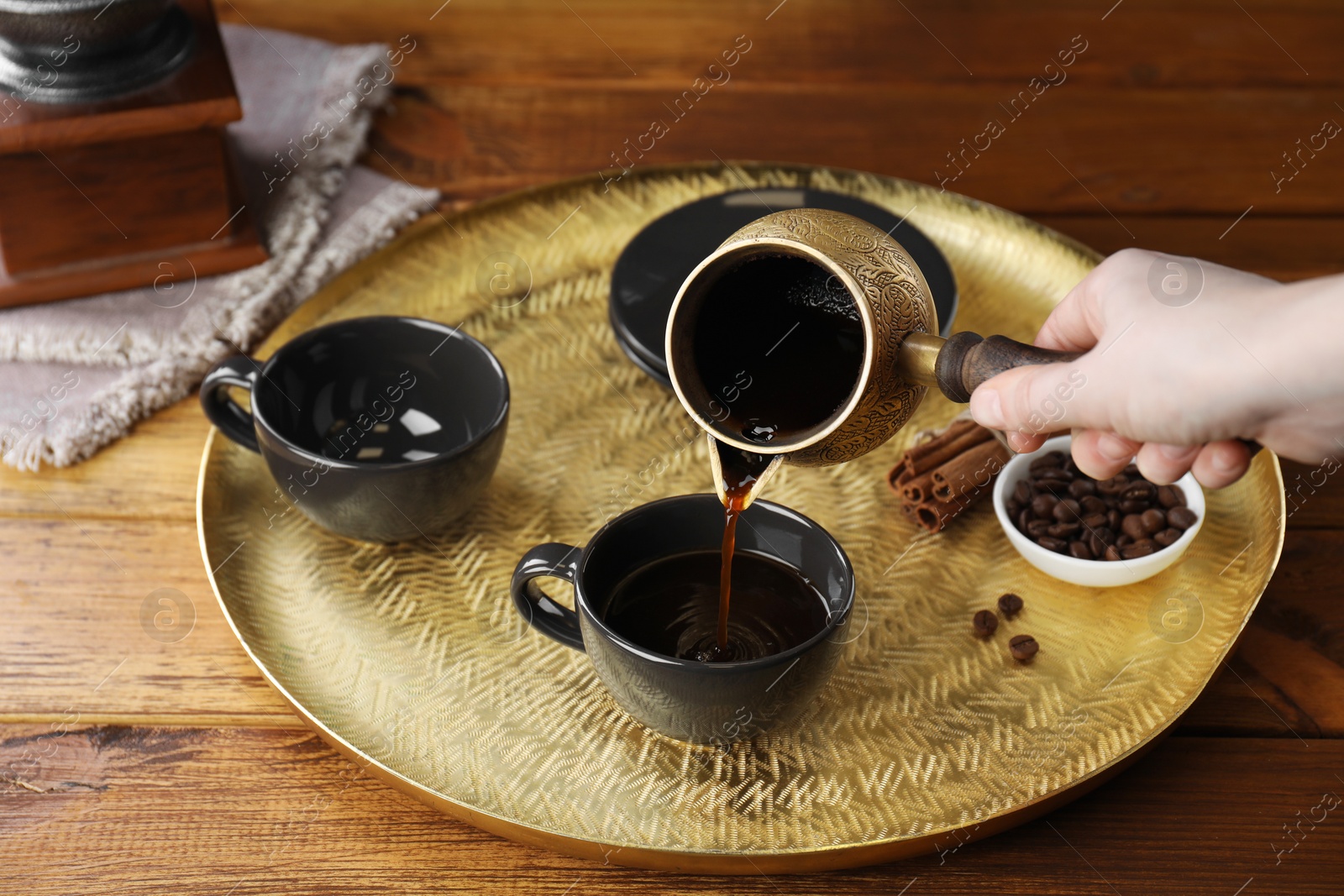 Photo of Turkish coffee. Woman pouring brewed beverage from cezve into cup at wooden table, closeup