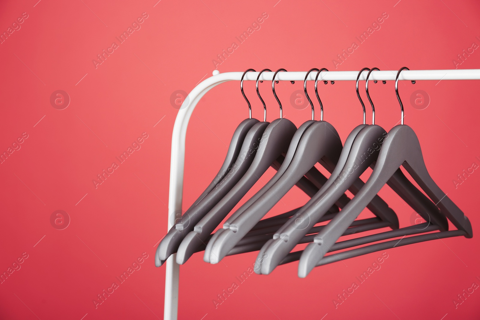 Photo of Empty clothes hangers on metal rack against color background. Space for text