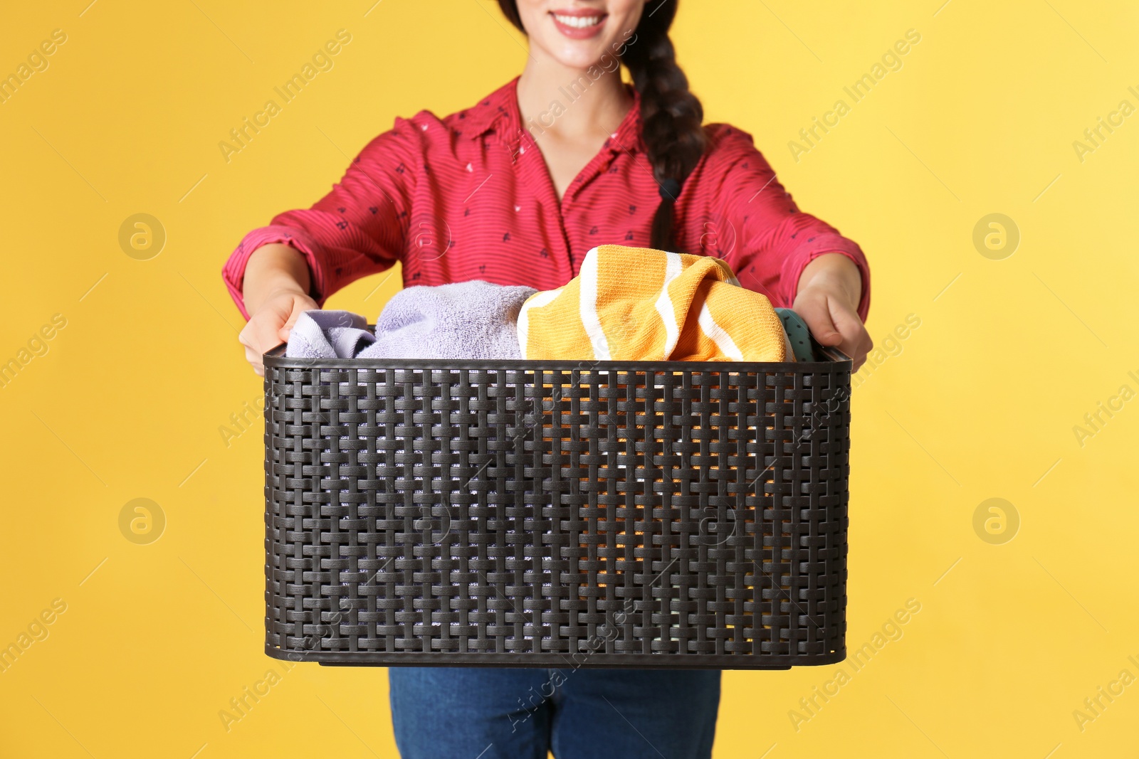 Photo of Young woman holding basket with clothes on color background, closeup