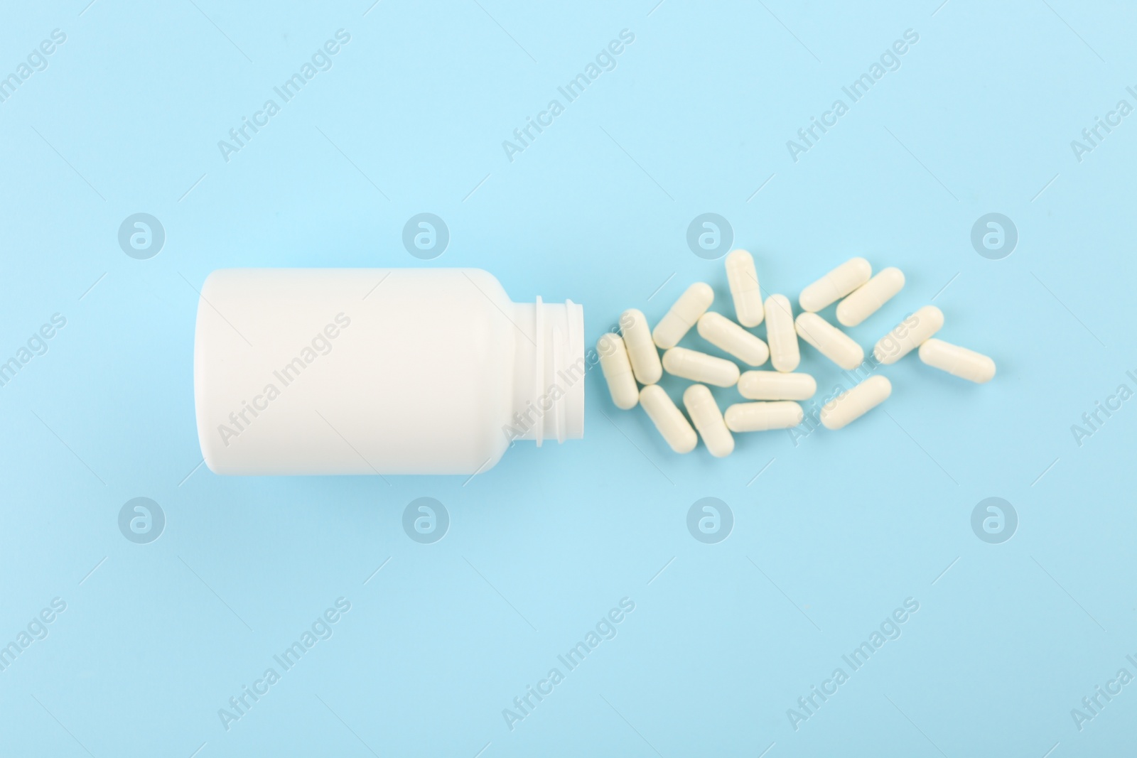 Photo of Bottle and vitamin capsules on light blue background, top view