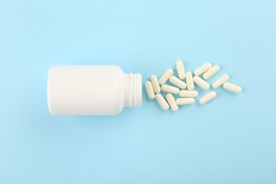 Bottle and vitamin capsules on light blue background, top view