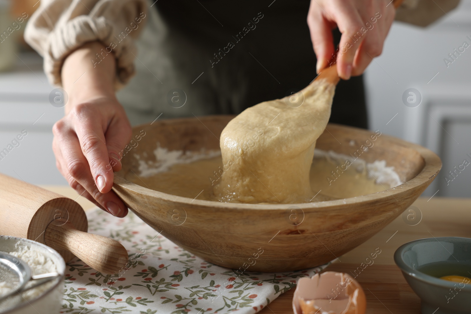 Photo of Woman kneading dough with spoon in bowl at wooden table indoors, closeup