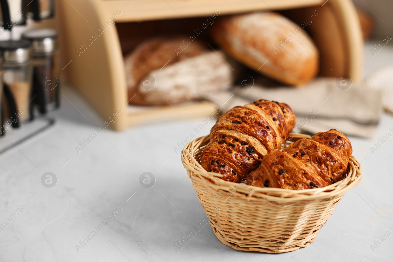 Photo of Wooden bread basket with freshly baked loaves and croissants on white marble table in kitchen, space for text