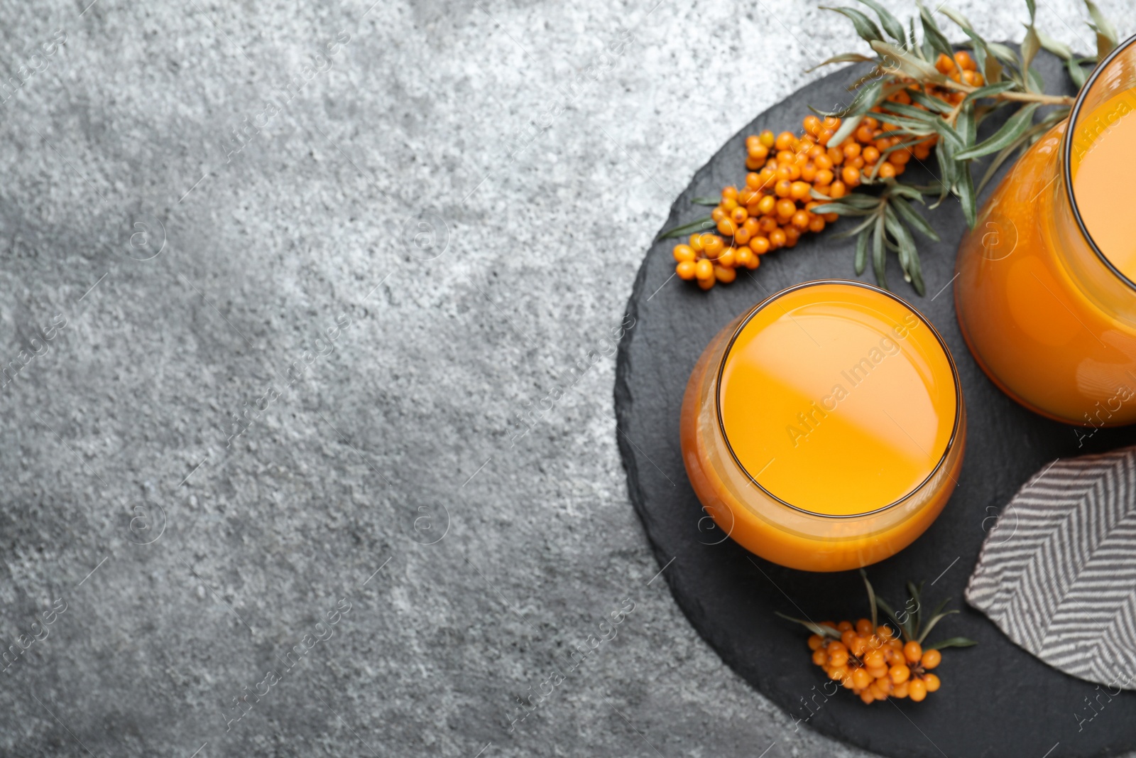 Photo of Delicious sea buckthorn juice and fresh berries on grey table, top view. Space for text